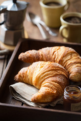 Good morning concept - Freshly baked croissants on a tray with a small jar of jam and two cups of...