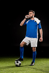 handsome man in uniform standing with towel on shoulder and drinking water from bottle isolated on...