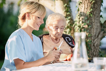Pflegerin hilft Seniorin beim schälen von Obst