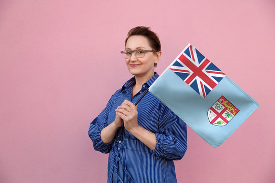 Fiji flag. Woman holding Fijian flag. Nice portrait of middle aged lady 40 50 years old holding a large flag over pink wall background on the street outdoor.