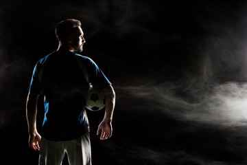 silhouette of football player holding ball on black with smoke