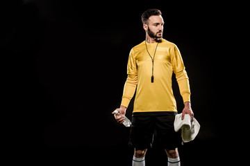 handsome referee holding bottle with water and towel in hands isolated on black
