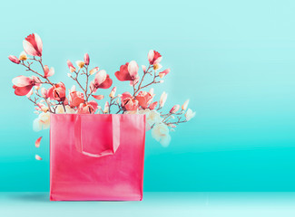 Pink shopping bag with spring blossom branches standing at turquoise blue background. Trendy color....