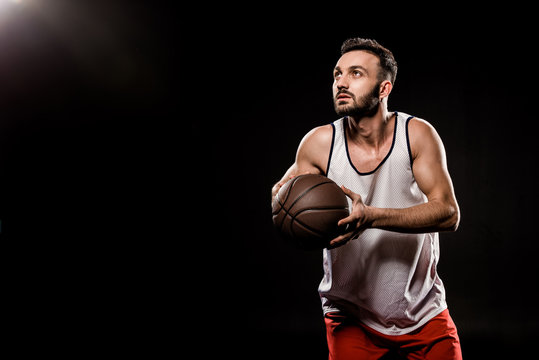 serious basketball player holding ball on black background
