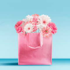 Pastel pink shopping bag with gerbera daisies flowers bunch standing on table at turquoise blue wall background. Branding mock up. Copy space. Summer love, sale and promotion concept