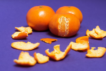 Three tangerines on purple background. Delicious mandarins surrounded by peels closeup.