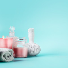 Spa beauty background with tools: cream, towels, burning candles, massage herbal stamp standing on pastel blue table. Salon wellness therapy treatments and equipment. Body care and beauty concept