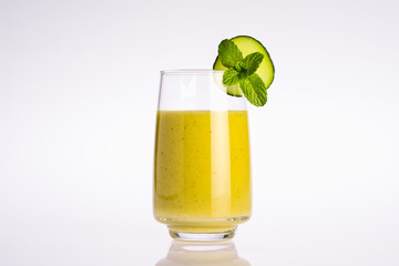 glass of green and yellow organic vegetable juice with slice of cucumber and mint leaf on white background