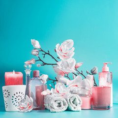 Spa beauty background with tools: cream, towels, serum, burning candles, lotion , standing on pastel blue table with white pink blossom flowers . Salon wellness therapy treatments and equipment.