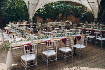in the wedding banquet area there are tables and transparent chairs, on the tables there are plates, glasses, cutlery and compositions from green branches and candles