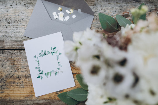 on the old wooden table lies an envelope and invitation card, next to it lies a bouquet of white flowers with greenery