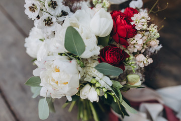 on the vintage floor of old wooden planks there is a bouquet of white flowers, red flowers, twigs and greenery tied with a ribbon