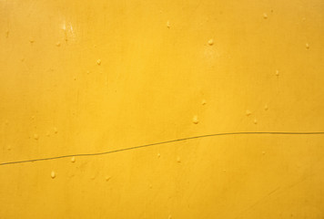 Wet yellow metal surface in drops of rain abstract background texture close up