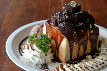 Honey toast ice cream with banana sliced and whipped cream top with brownie served on white plate over wooden table