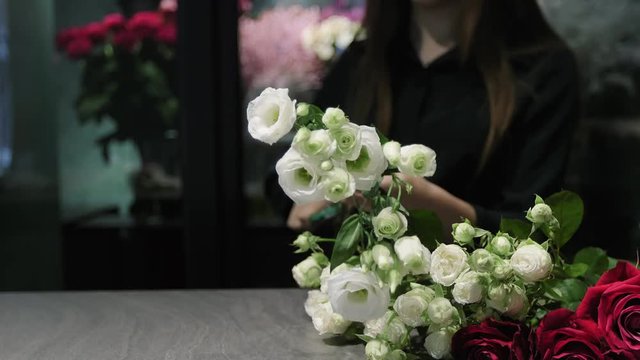 Professional florist cuts white and red roses with a pruner over the table, woman's hands close-up.