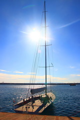 Sailing boat in prot of Rijeka, Croatia; sun on blue sky in background