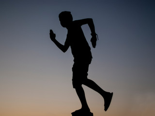 Fototapeta na wymiar silhouette of a person boy running towards sunset sky background. Man in shorts and tank top silhouette.