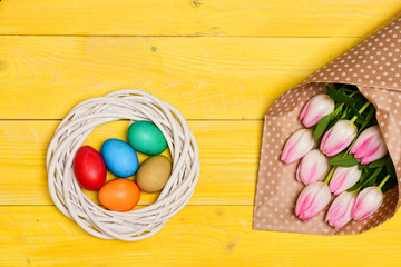 Easter eggs symbol. Spring vibes. Easter is coming. Colorful bright eggs and bouquet fresh tulip flowers on yellow background top view. Spring holiday. Tradition celebrate easter. Happy easter season