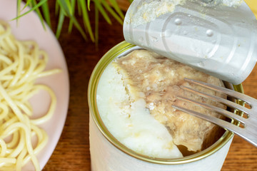 A tin, can of canned meat with a folk in it, italian pasta on a plate close up