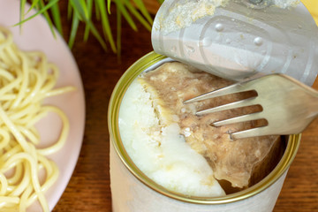 A tin, can of canned meat with a folk in it, italian pasta on a plate close up