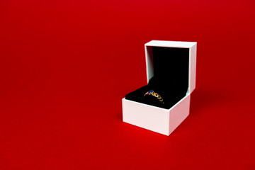 Beautiful golden ring with blue gemstone in the white box isolated on red background. Luxurious engagement ring. Present