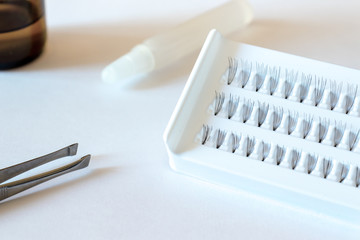 Eyelash extension, beauty and cosmetology concept - set of false eyelashes, glue and tweezers on white table