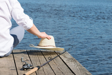 closeup of fishing rod and hat of a fisherman against a background of blue water