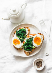 Fototapeta na wymiar Fried spinach, cream cheese and soft boiled eggs sandwiches - delicious healthy breakfast or snack on a light background, top view