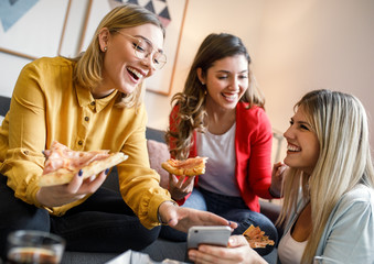 Three female friends chatting and enjoying eating pizza at home.