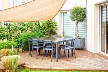 Foto op Canvas Modern outdoor wooden terrace with dining table, chairs and a shade sail © Delphotostock