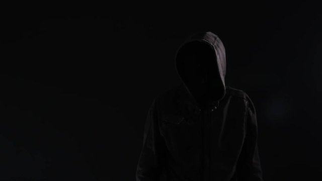 Unrecognizable hooded criminal gesturing finger on lips or shh sign to silence the victim of his crime act