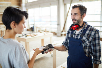 Lady customer using modern smartphone and putting it to terminal while paying handsome bearded...