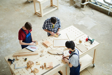 High angle view of concentrated carpenters standing at table and working with wood while making...