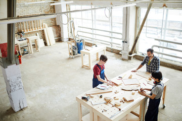 Workspace of carpenters: serious busy workers standing at one table and making wooden toy together in workshop