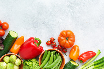 Fresh raw ingredients tomatoes cucumbers lettuce pepper spring onion broccoli peas on the white table, top view, copy space, selective focus