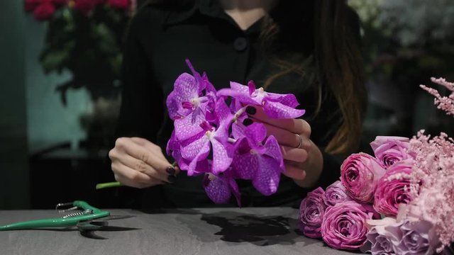 Professional woman florist makes the bouquet from pink flowers tulips, roses, orchids and solidago.