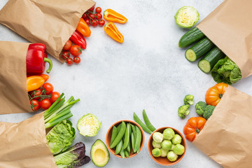 Fresh raw ingredFresh raw farm produce in paper bags, tomatoes cucumbers lettuce pepper spring onion broccoli peas on the white table, top view, copy space, selective focusients for salad