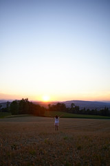 Beautiful classic shot of a little girl in a white dress walking on the hills of a field in spring sunset