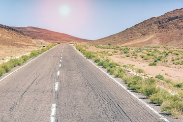 An arid hot desert with mountains and a road under a blue sky.