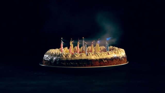 studio shoot of burning candles blowing out on birthday cake on black background