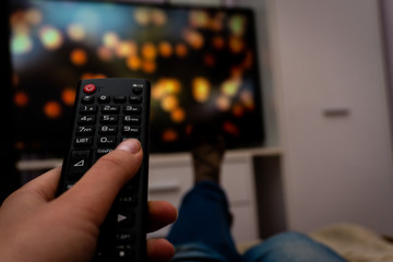 Female holding TV remote control in front of TV. Couch potatoe. Point of view shot.