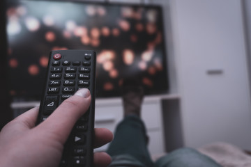 Female holding TV remote control in front of TV. Couch potatoe. Point of view shot.