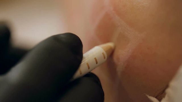 Close-up beautician draws the contours of a white pencil on the face of the patient. Schematic marking before contouring. Close-up preparation of the face for cosmetic plastic surgery.