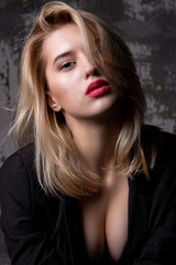 Fototapeta na wymiar Portrait of seductive blonde model wearing jacket with decollete posing at studio with shadows