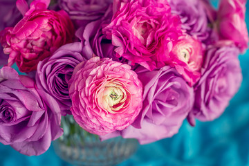 Fototapeta na wymiar Pink ranunculus flowers and purple roses close-up in a vase on a blue background.
