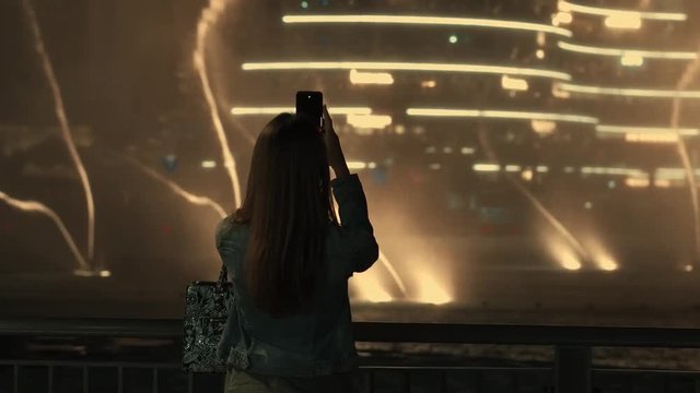 Back view of woman with smartphone taking a picture of dancing fountains show