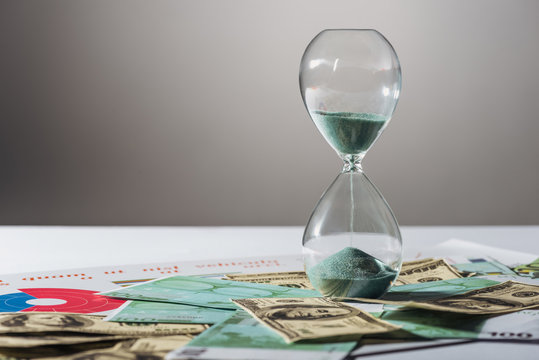 hourglass on dollars and euros banknotes with grey background