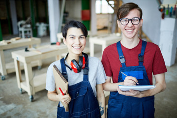 Cheerful satisfied young students in workwear standing in modern carpentry classroom and laughing...