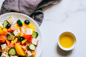 Top view greek salad of fresh cucumber, tomato, sweet pepper, red onion, feta cheese and olives with olive oil on marble.