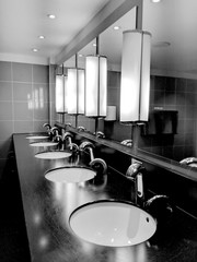 Row of shiny, contemporary, ceramic wash hand basins in front of a wall of top lit mirrors, in...